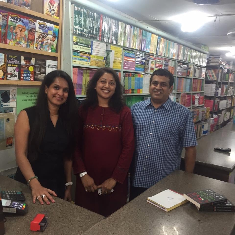 Visitors smiling inside Maneesh Book Shop beside shelves of books